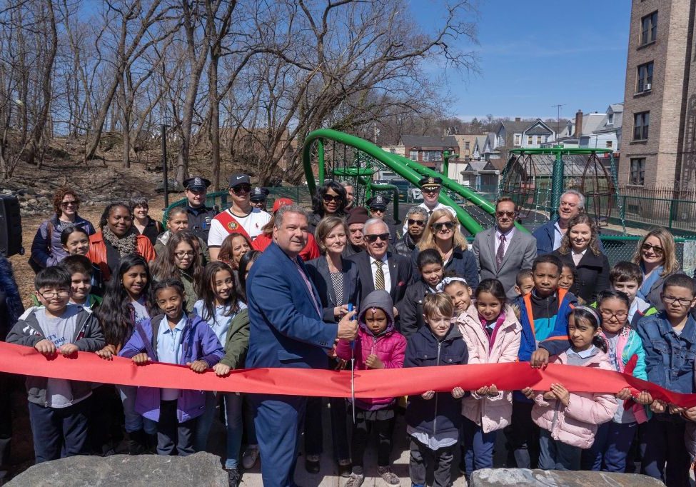 Man cutting red ribbon with group of people behind him